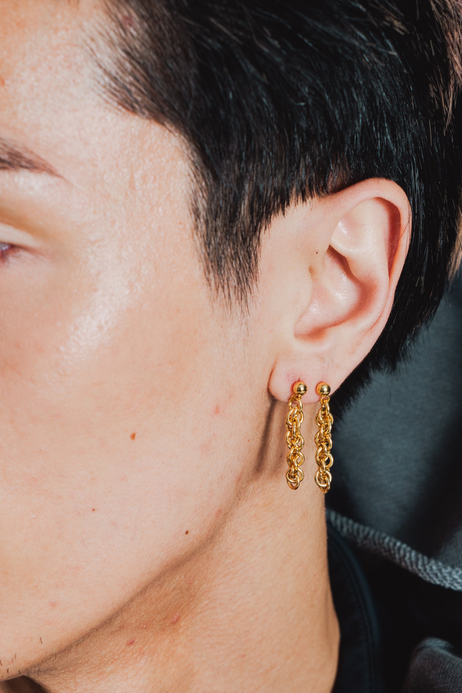 Two gold tone chainlink earrings on model's ear